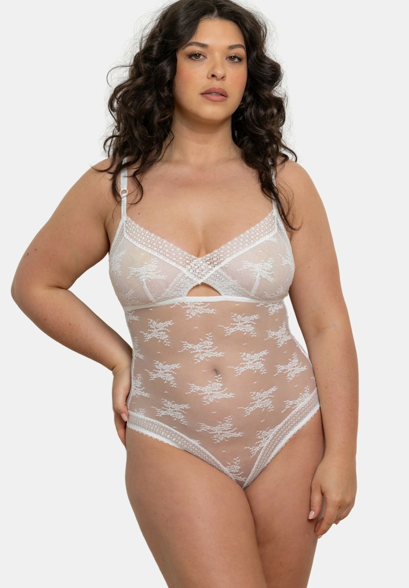 Body en dentelle blanche transparente avec des motifs floraux, présentant un design croisé à l'avant et des finitions délicates. Bretelles ajustables et coupe ajustée.