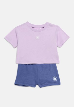 Kortærmet lilla crop top med stjerne-logo kombineret med blå shorts med elastisk taljebånd og Converse All Star-print på benet.