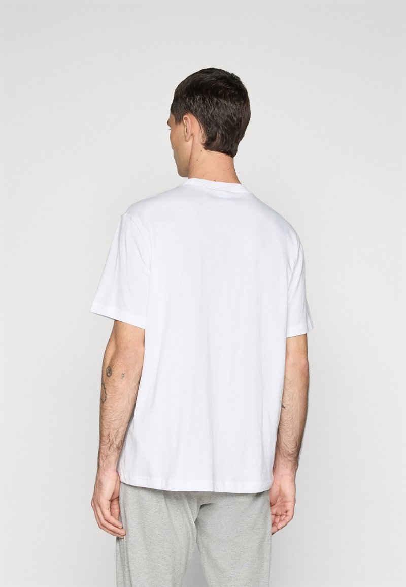 Camiseta blanca de algodón con mangas cortas y cuello redondo, con un dobladillo recto y un diseño minimalista, vista desde la parte trasera.