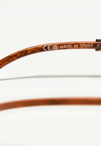 Bruna sköldpadds solglasögon med en slät yta. Den inre delen av skalmen visar "CE UK CA MADE IN CHINA" i vit text.