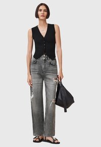 Zwarte geribbelde mouwloze top met knopen, gecombineerd met versleten grijze wijde jeans. Houdt een zwart leren tas vast. Platte zwarte sandalen.