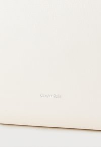 Λευκή δερμάτινη θήκη με υφή, με ανάγλυφο λογότυπο "Calvin Klein" σε διακριτικό, ανοιχτόχρωμο χρώμα.