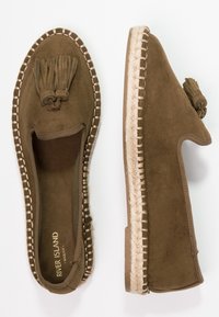 Braune Wildleder-Espadrilleslipper mit einem fransigen Akzent, gewebten Jute-Mittelsohlen und kontrastierenden Nähten entlang der Kanten.