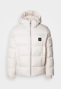 Veste d'hiver blanche matelassée avec capuche, fermeture éclair frontale et écusson logo sur le côté gauche de la poitrine.