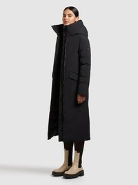 Abrigo largo negro acolchado con cuello alto, bolsillos laterales y cierre de cremallera. El modelo lo combinó con botines beige y medias negras.