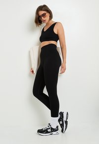 Top corto nero e leggings a vita alta in un tessuto liscio e stretch. Accentuati da calze sportive bianche e sneakers nere.