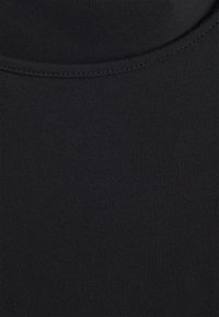 Černá bavlněná tkanina s hladkou strukturou. Má zaoblený výstřih a šití podél okraje. Žádné vzory ani zvýraznění.