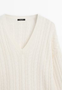 Maglione beige a trecce con scollo a V profondo, caratterizzato da motivi testurizzati e polsini a coste. Etichetta con scritto "Massimo Dutti."