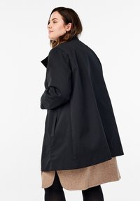 Cappotto impermeabile nero con una vestibilità rilassata, maniche lunghe e tasche laterali, caratterizzato da un design minimalista e una texture liscia.