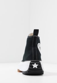 Black high-top sneaker with white stitching, thick white sole, star detail on heel, and logo patch on the side, shown from the back.