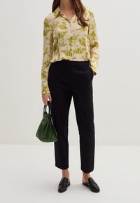 Blusa leggera e a fantasia con design di foglie verdi, abbinata a pantaloni neri su misura. Completata con una piccola borsa verde e mocassini neri.