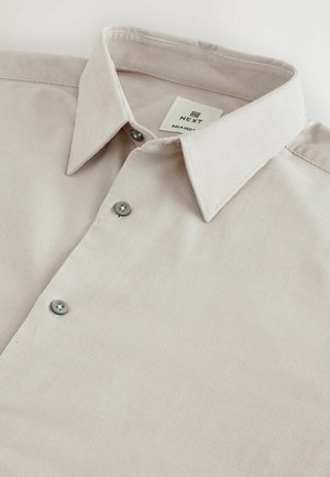 Heledbeez värvi nööpidega särgil on tekstureeritud kangas, terava kraega ja hallid nööbid esiosas. Silt ütleb "NEXT RELAXED".