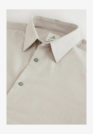 Svetlo béžová košeľa na gombíky s textúrovanou tkaninou, so špicatým golierom a šedými gombíkmi pozdĺž prednej časti. Štítok hovorí "NEXT RELAXED."