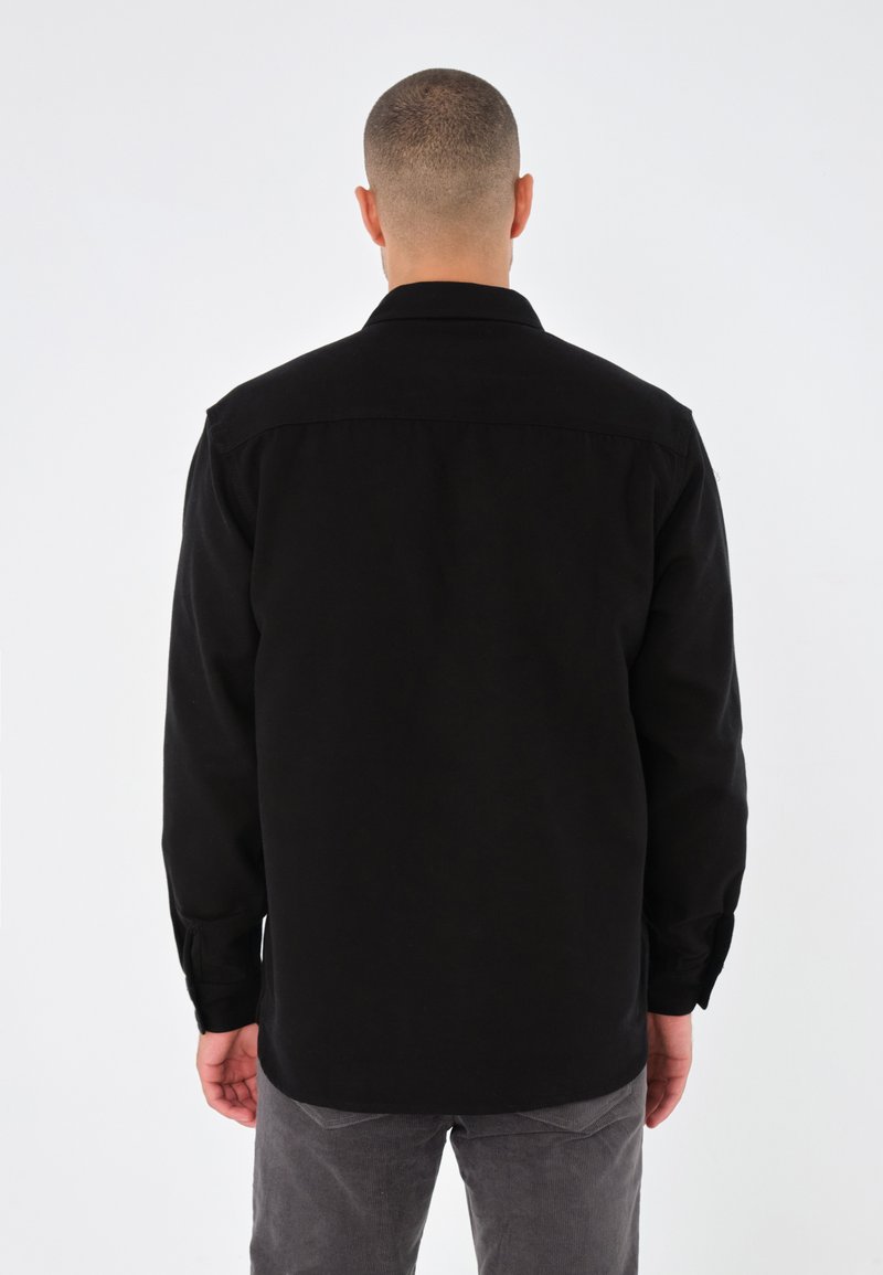 Camisa negra de manga larga hecha de algodón con cuello abotonado, con dobladillo recto y puños de un solo botón. Vista trasera mostrada.