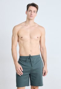 Mørkegrønne shorts laget av teksturert stoff; har elastisk midje med snor og sidelommer. Enkelt design, kne-lengde snitt.