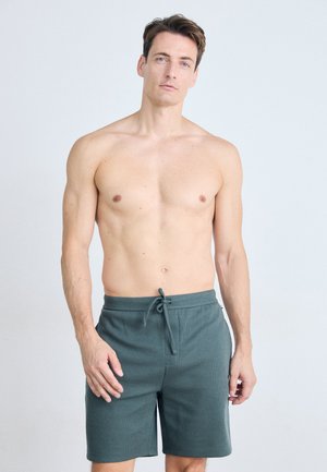 Dunkelgrüne Shorts aus strukturiertem Stoff; ausgestattet mit einem elastischen Bund mit Kordelzug und seitlichen Taschen. Schlichtes Design, knielanger Schnitt.