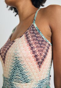 Multicolored tank top featuring a diamond pattern in shades of peach, brown, and green, with thin adjustable straps and smooth texture.