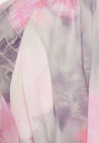 Tissu en chiffon dans des tons doux de rose et gris, présentant un motif floral. Détail froncé avec des accents fins gainés le long du bord.