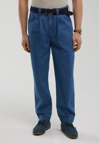 Mėlynos juostuotos kelnės, pagamintos iš austos medžiagos, pasižyminčios laisvu siluetu, prisiūtomis apačiomis ir tamsiai mėlynu diržu. Tekstūruota paviršius su vertikaliomis baltomis juostelėmis.