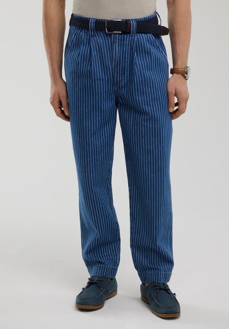 Mėlynos juostuotos kelnės, pagamintos iš austos medžiagos, pasižyminčios laisvu siluetu, prisiūtomis apačiomis ir tamsiai mėlynu diržu. Tekstūruota paviršius su vertikaliomis baltomis juostelėmis.