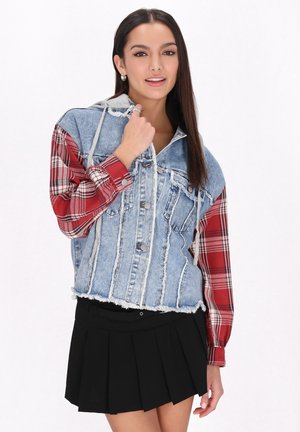 Giacca in denim e plaid con orlo strappato, dotata di cappuccio, chiusura con bottoni e maniche a quadretti rossi e bianchi. Abbinata a una gonna nera plissettata.