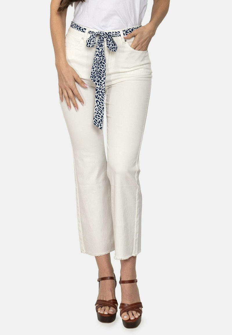 Pantalones blancos cortos con un cinturón de lazo de estampado de leopardo azul, con un dobladillo deshilachado y un ajuste slim. Combinados con sandalias de plataforma marrones.