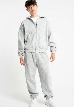 Szara bluza z zamkiem błyskawicznym i prążkowanymi mankietami, w połączeniu z dopasowanymi szarymi dresami. Miękka tkanina, luźny krój, minimalistyczny design. W komplecie białe sneakersy.