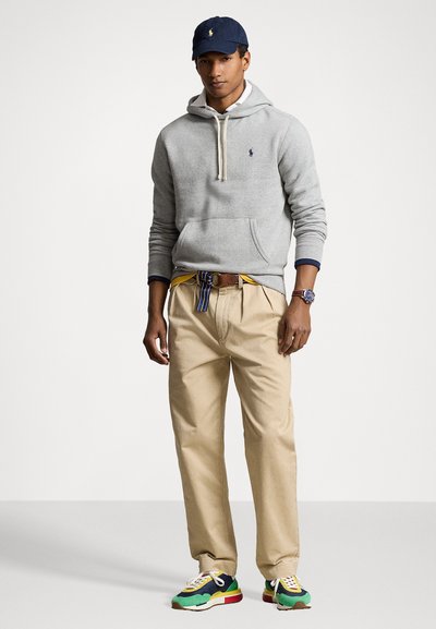 Grå hættetrøje med snøre, khaki bukser, multicolor sneakers og marineblå cap. Har broderet logo på hættetrøjen og stribet bælte.