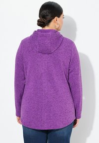 Lila huvtröja med en texturerad, melerat mönster. Långa ärmar, en avslappnad passform och rundad nederkant. Buren med mörkblå jeans.