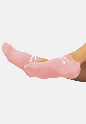 Pink ankle socks made of soft fabric, featuring textured material and white "BEACH" text near the top for visibility.