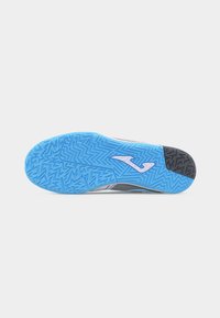 Semelle en caoutchouc bleue d'une chaussure de sport avec un motif de bande de roulement en zigzag et un logo blanc près de la voûte plantaire, photographiée sur un fond blanc.
