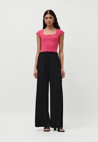 Tett rosa ribbestrikket topp med korte ermer og firkantet halslinje, kombinert med svarte plisserte vide bukser med elastisk midje.