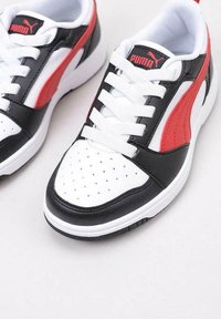 Scarpe sportive in bianco e nero con accenti rossi, caratterizzate da una finitura in pelle liscia, punta perforata e lacci bianchi. Logo PUMA visibile.
