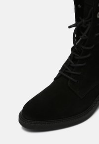 Stivale alla caviglia in suede nero con punta rotonda, cuciture evidenti e lacci. Presenta una superficie testurizzata e una suola in gomma a profilo basso.
