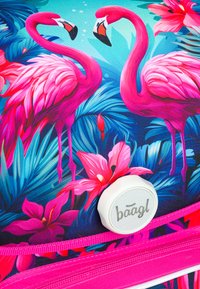 Batoh s motivem plameňáků má růžový a modrý tropický design, kulatou nášivku a jasně růžové detaily na zipu. Odolný textilní povrch.