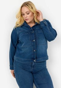 Tumši zila džinsu jaka ar divām priekšējām kabatām, pogu aizdari un garām piedurknēm. Ievērojami šuvju detaļas ap kabatām.