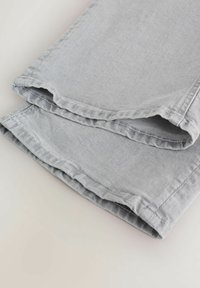 Lysegrå denimjeans foldet for at vise kanterne med dobbel syning på en neutral baggrund.