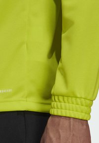 Neon-gelbes Langarmshirt aus strukturiertem Stoff, mit elastischen Bündchen und einem dezenten Markenlogo am Saum.