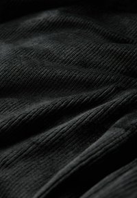 Schwarzer, strukturierten Stoff mit gerippten Mustern, der einen subtilen Glanz und eine weiche, plüschige Oberfläche aufweist. Sanfte Drapierung über die Falten des Stoffes.