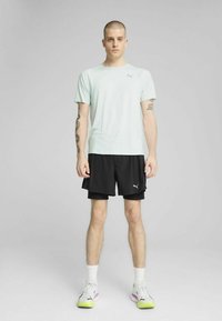 Lysgrøn kortærmet skjorte med et logo på brystet, parret med sorte shorts. Sættet er komplementeret af hvide sneakers med farverige accenter.