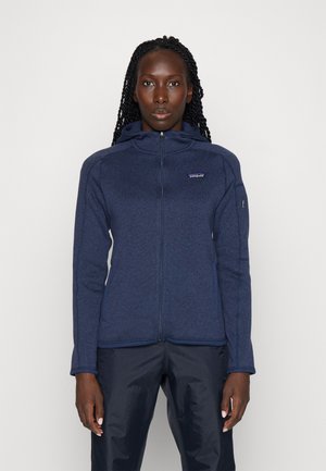 Chaqueta de zip azul marino hecha de forro polar texturizado, con un cuello alto, bolsillos laterales y un parche de logo en el pecho.