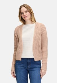 Roze gebreide cardigan met open voorkant, geribbelde boorden, een textuurpatroon en zachte garen. Gedragen over een gestreepte lange mouwen shirt en blauwe jeans.