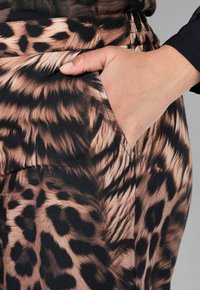 Tkanina s leopardím vzorem v odstínech hnědé a černé, se boční kapsou a hladkým povrchem. Zdůrazňuje tvar a design oděvu.
