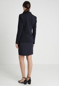 Námořnický blazer a sukně, střižený střih, hladká tkanina, dlouhé rukávy s detaily knoflíků, doplněno černými lodičkami.