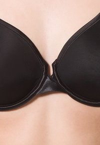 Sostenitore imbottito nero con superficie liscia e coppe sagomate. Presenta un centro anteriore e spalline regolabili. Sottogola testurizzato per supporto.