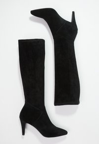 Mustat mokkanahkasaappaat, jotka ulottuvat polveen, ovat teräväkärkiset ja niissä on korkea, kapea korko, sekä sileä pinta. Saappaissa on geometrinen kuvio nilkassa.