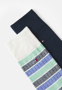 Deux paires de chaussettes en coton : l'une marine, l'autre blanche avec des rayures vertes et bleues, arborant un petit logo dans le motif.