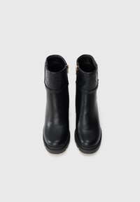 Botas de tobillo de cuero negro con una banda negra texturizada en la parte superior, con cremalleras doradas a ambos lados y una suela de goma para mayor tracción.