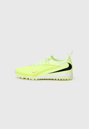 Limettengrüne Sportschuhe mit schwarzen Akzenten, strukturiertem Obermaterial, flacher Sohle mit kleinen Noppen und pinkem Branding an der Seite.