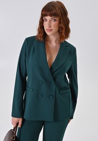 Teal dubbelzijdig blazer gemaakt van gladde stof, met een diepe V-hals, twee zakken en knoopaccenten, gestyled met bijpassende broek.